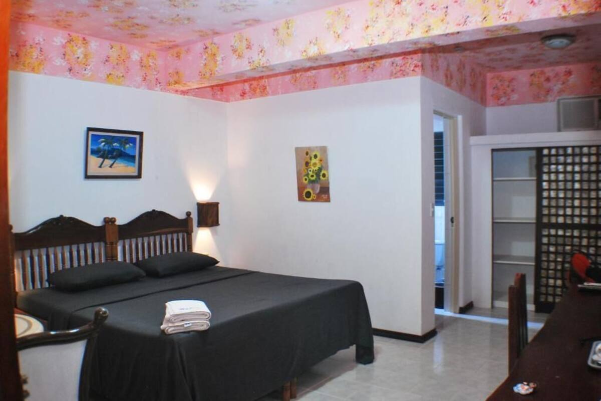 A bedroom with a bed, a nightstand, a wall-mounted lamp, and a door leading to a bathroom.