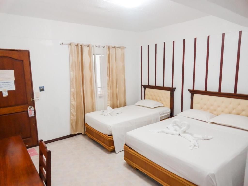 A hotel room with two beds, a wooden desk, and a window with curtains.