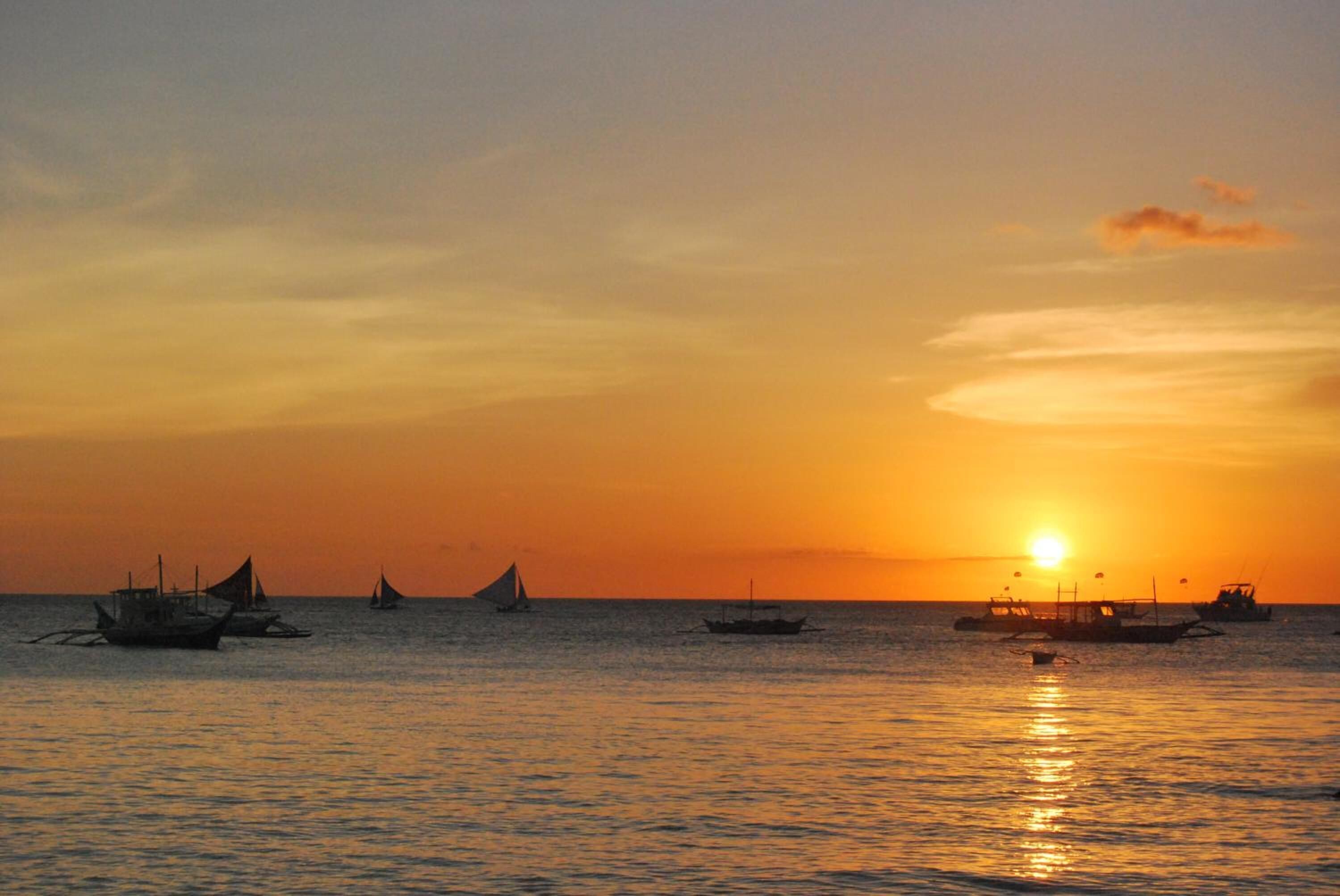 A sunset over the ocean with several boats.