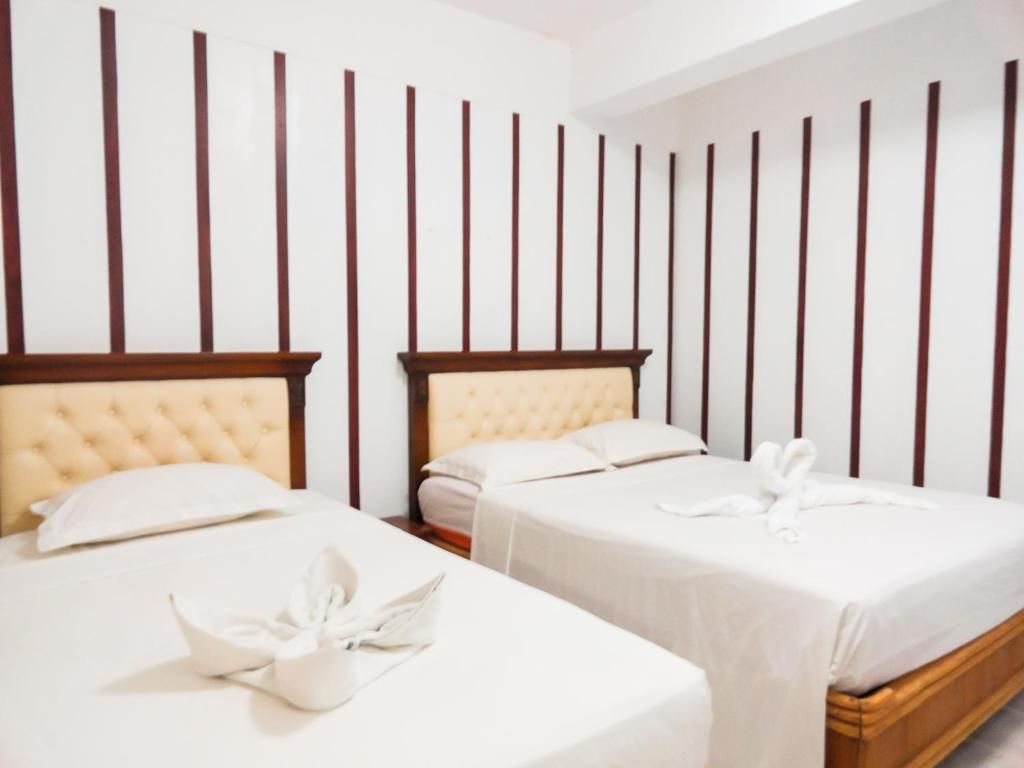 Habitación de hotel con dos camas, cada una con cabecero de madera y ropa de cama blanca.