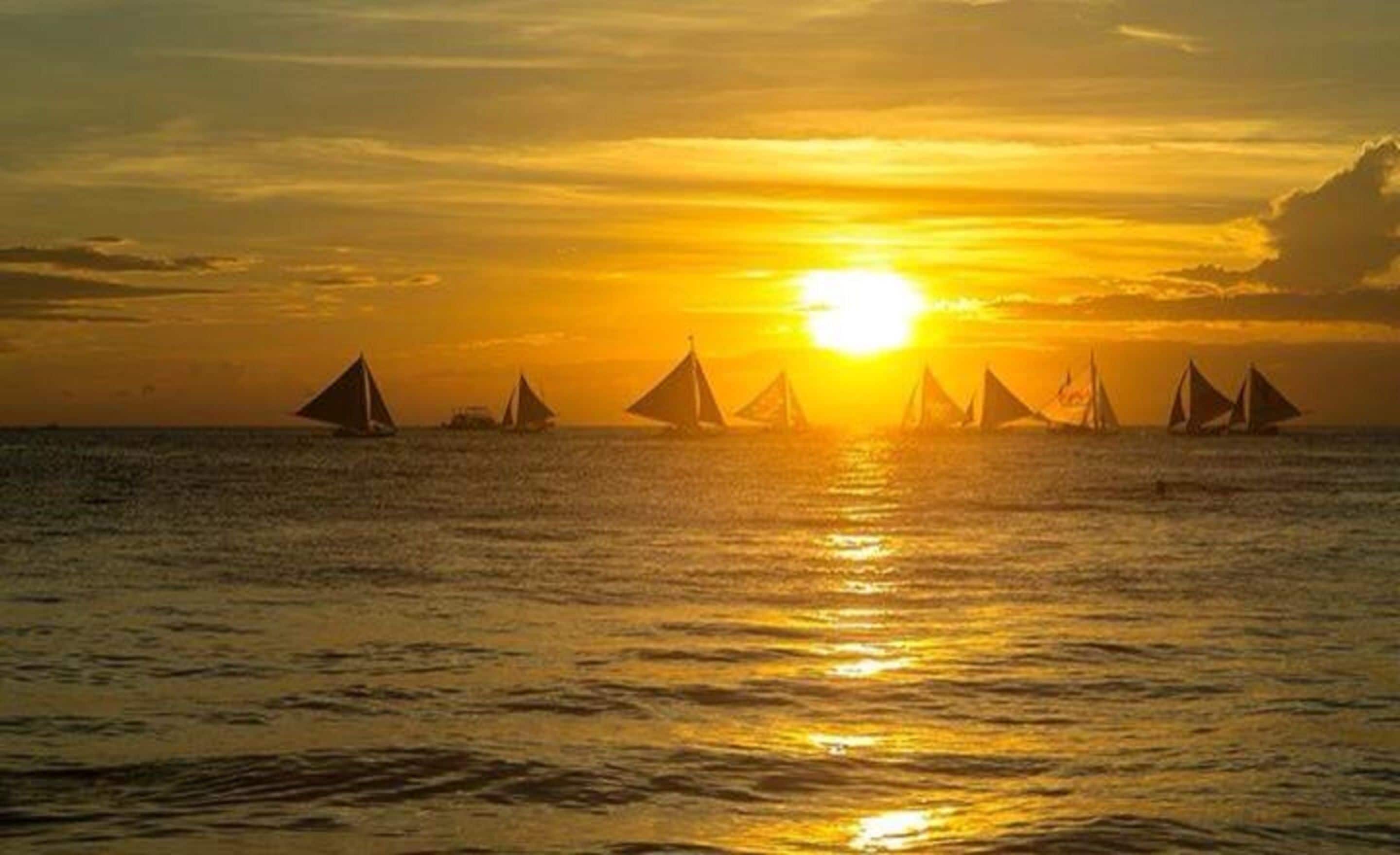 A sunset over the ocean with sailboats.