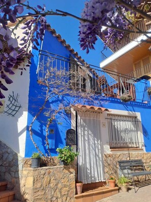 Une maison bleue avec un balcon, des marches en pierre et des plantes en pot.