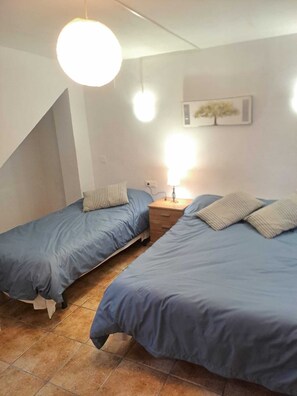 Une chambre avec deux lits simples, une table de chevet, une lampe et un luminaire au plafond.