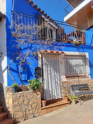 A blue building with a stone wall, a small porch, and a metal bench.