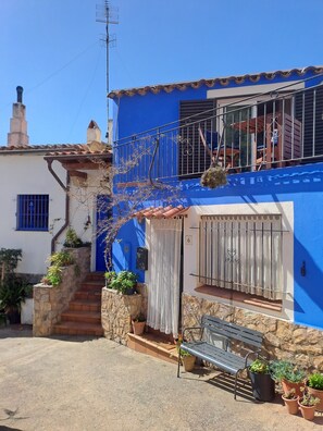 A two-story building with a blue facade, a balcony with metal railings, and a stone staircase leading to the entrance.