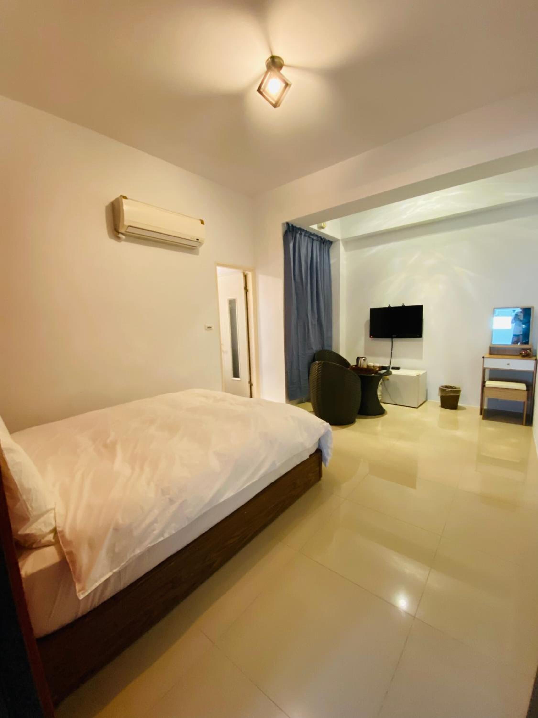 A hotel room with a bed, a desk with a computer, a TV, and an air conditioning unit.