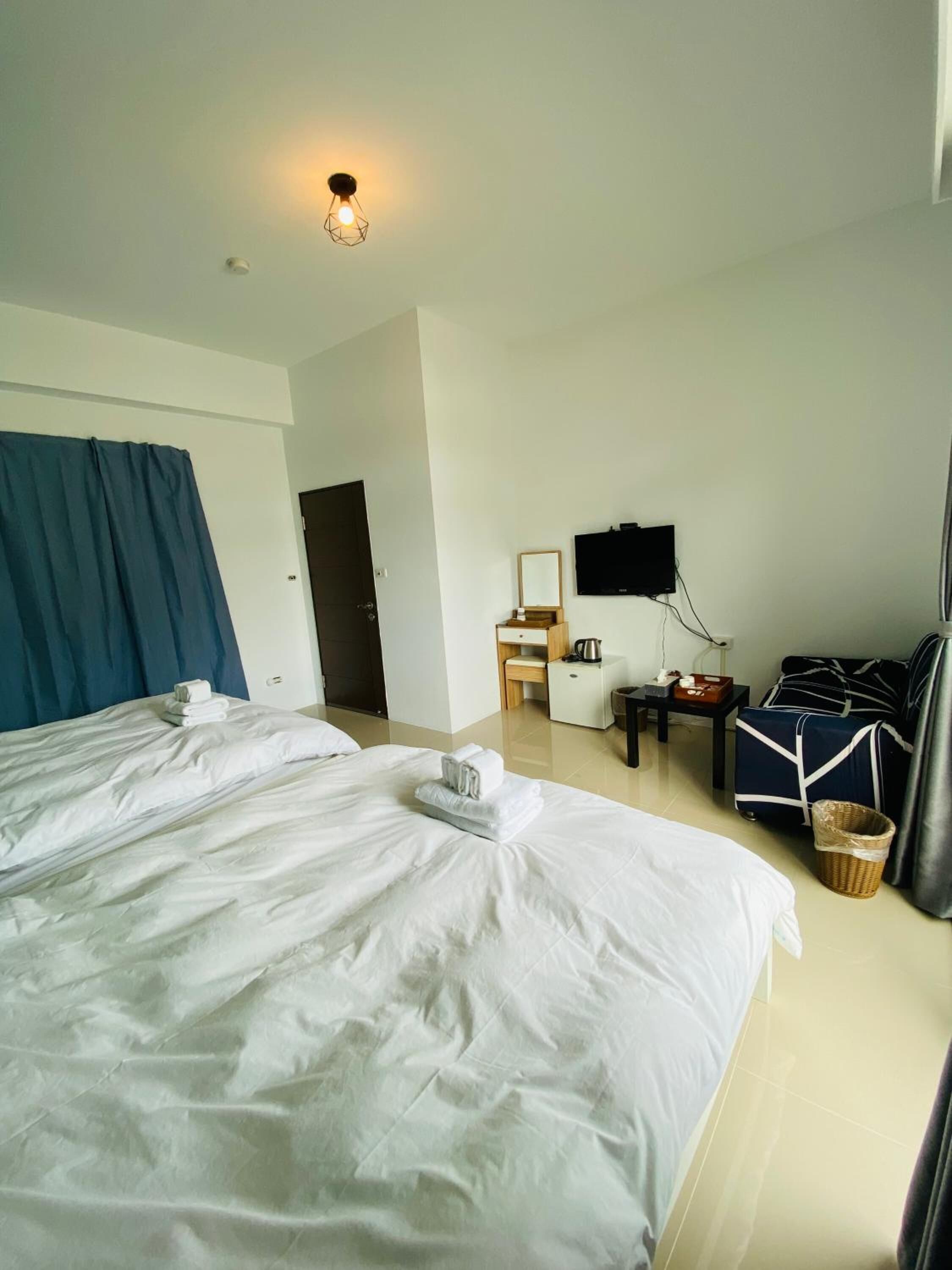 A hotel room with two beds, a flat-screen TV, a small desk with a chair, and a window with curtains.