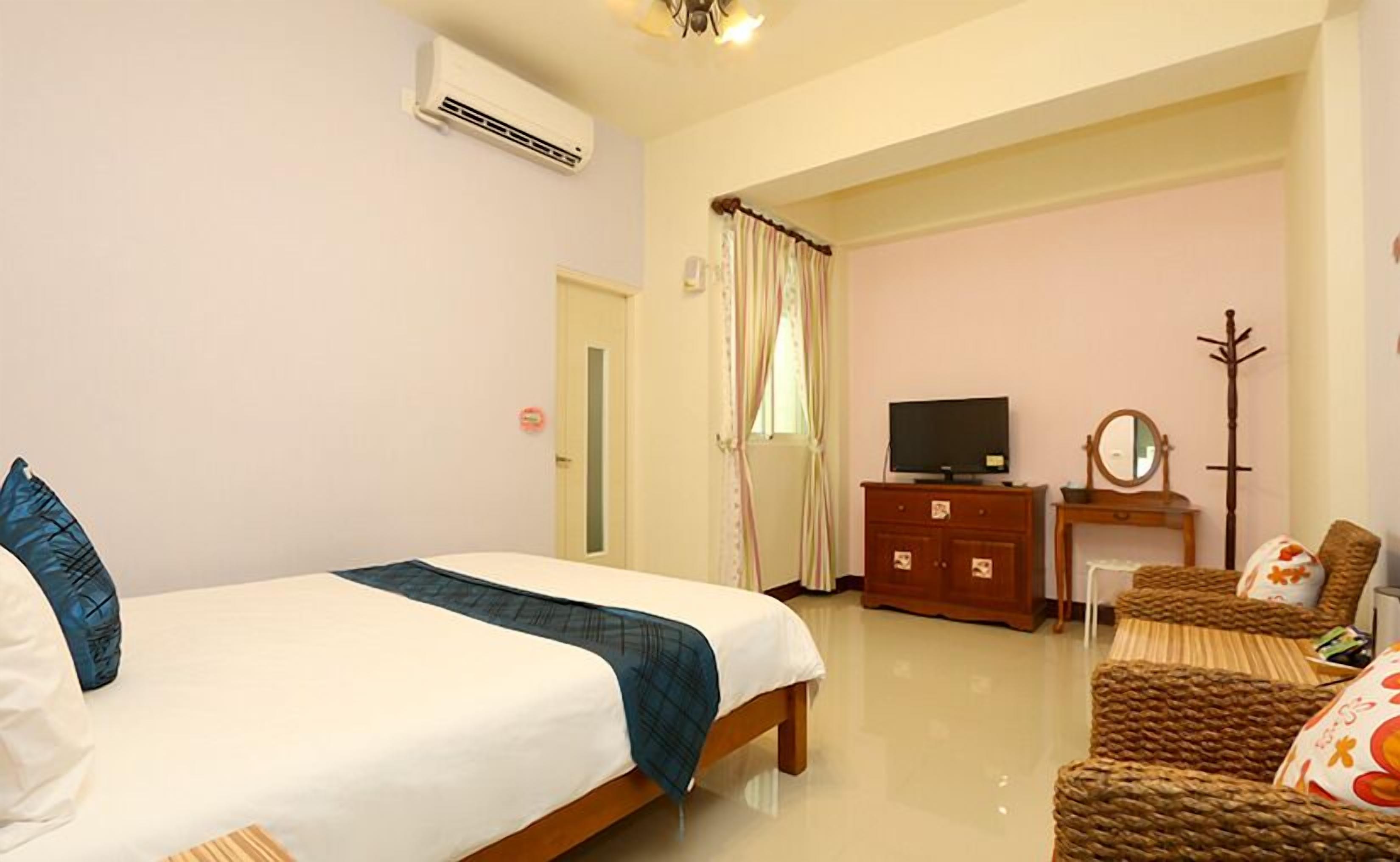 A hotel room with a bed, a dresser, a television, a coat rack, and a chair.