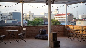 A rooftop terrace with a view of the city, featuring a brick wall, string lights, and foldable chairs. - Krit Hostel (Bangkok)