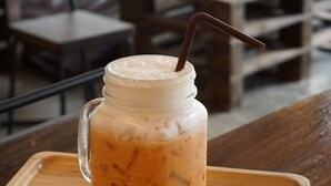 A mason jar with iced coffee on a wooden tray in a cafe setting. - Krit Hostel (Bangkok)