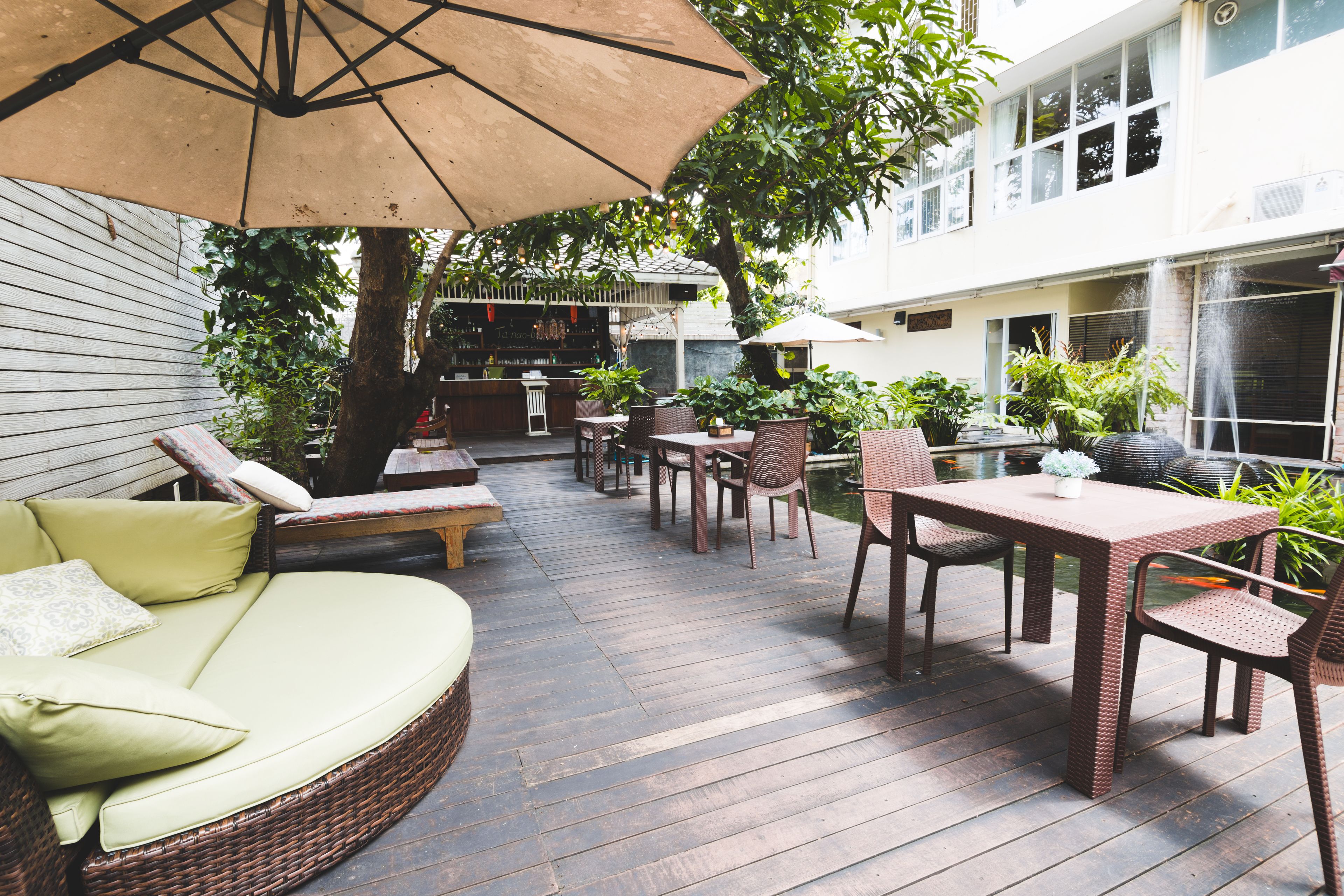 An outdoor patio area with wicker furniture, a table, and chairs. There is a large umbrella providing shade.