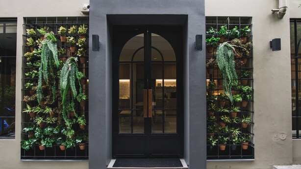 A building entrance with a black door, potted plants on either side, and a tiled floor. - Issara by d Hostel (Bangkok)