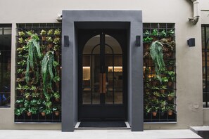 A building entrance with a black door, potted plants on either side, and a tiled floor. - Issara by d Hostel (Bangkok)