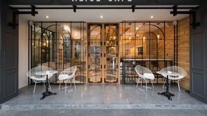 The entrance of Alice Cafe with glass doors, white chairs, and a wooden interior visible through the glass. - Issara by d Hostel (Bangkok)