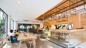 A modern cafe with a bar area, seating, and a view through the glass wall. - Issara by d Hostel (Bangkok)