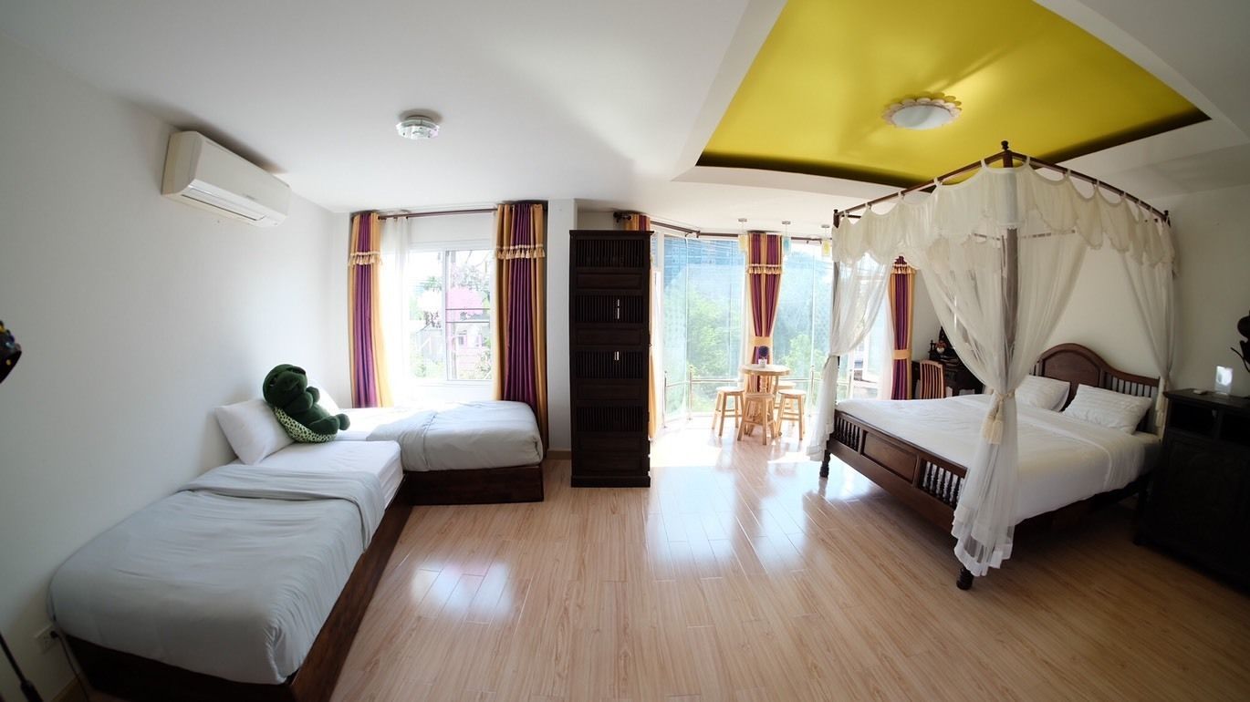 A hotel room with two single beds, a canopy bed, a small table with chairs, and a view of the outdoors.