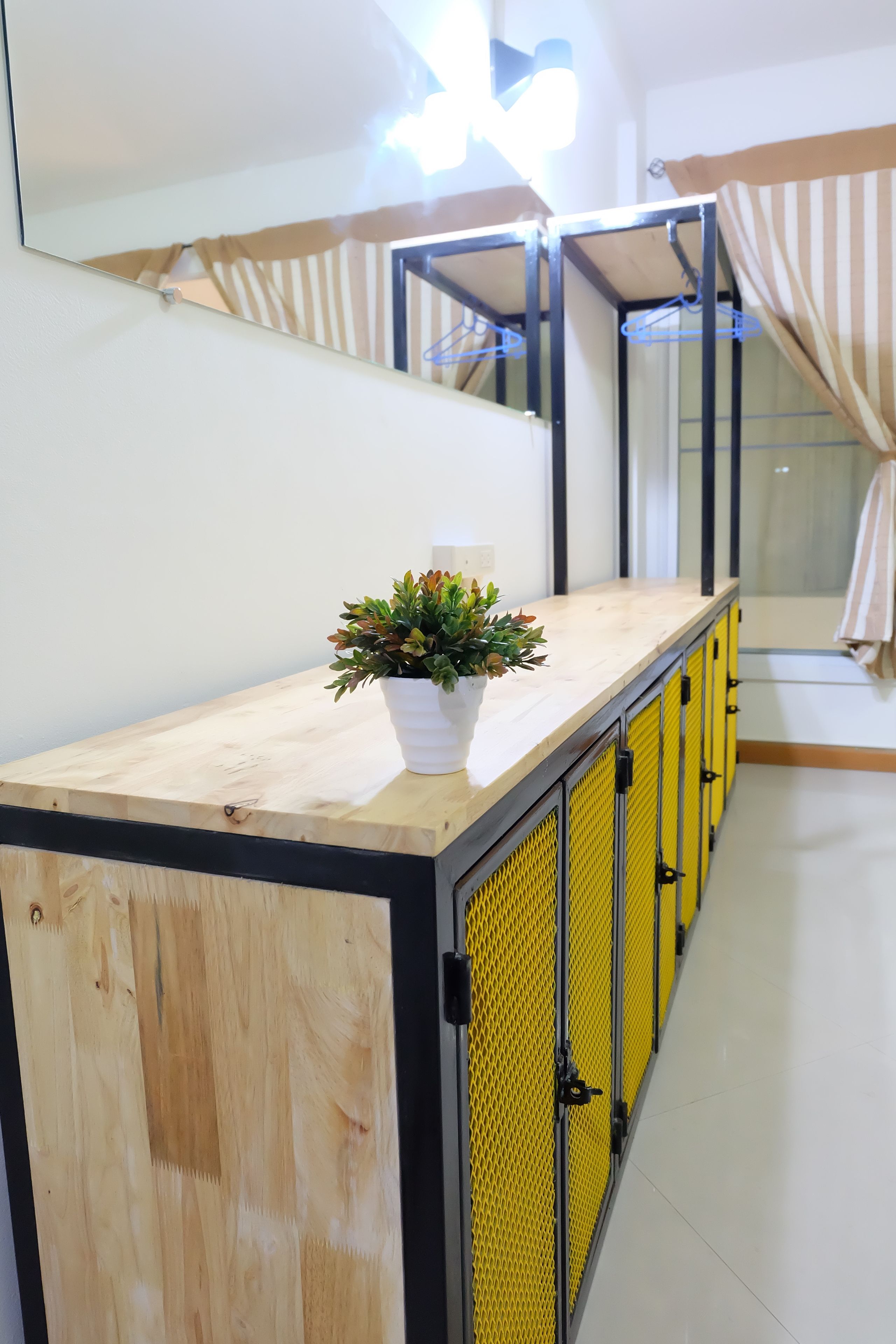 A wooden counter with a potted plant, yellow lockers, and a mirror reflecting a striped curtain.
