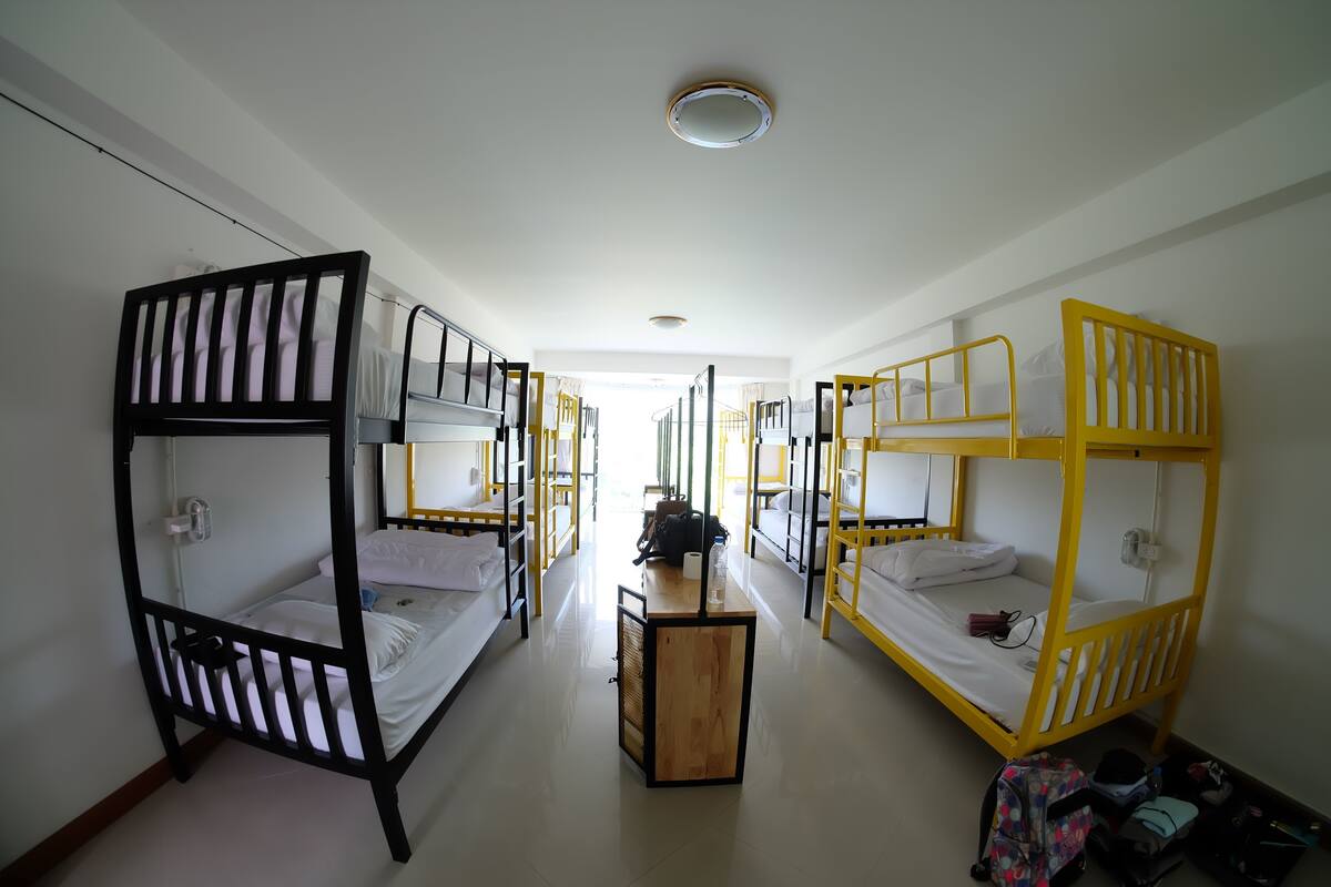 A dormitory room with bunk beds, a central desk, and a window.