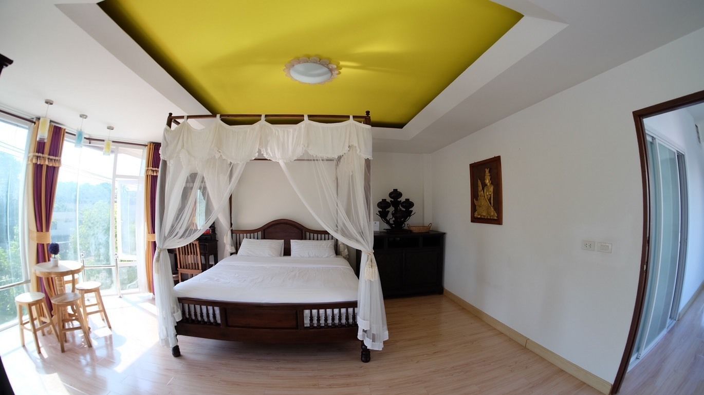 Een slaapkamer met een hemelbed, een geel plafond en een groot raam met gordijnen.