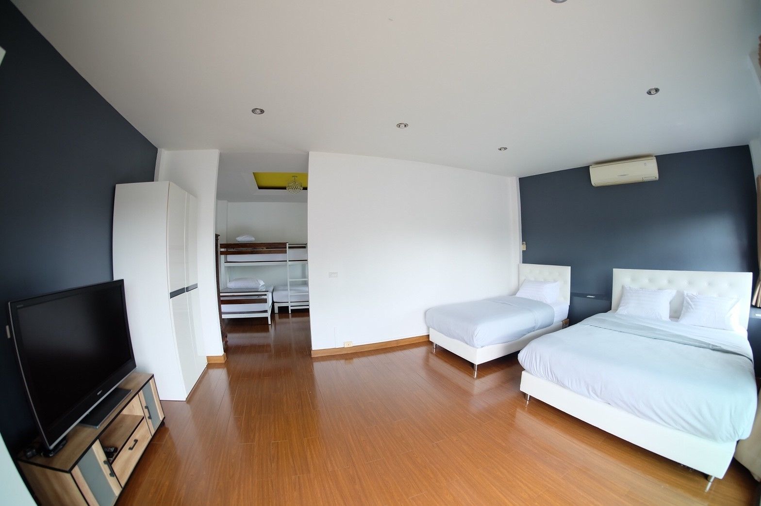 A modern hotel room with a wooden floor, a flat-screen TV, a bed with white bedding, and a small desk area.