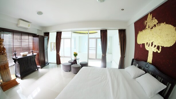 Habitación de hotel con una cama grande, un armario de madera, una mesita con un jarrón y vistas al exterior a través de amplios ventanales.