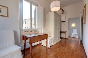 A room with a wooden floor, white furniture, a radiator, and a window with open shutters.