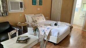 A bedroom with a bed, a desk, a chair, a small table, and a wall-mounted air conditioner. - Padthaway Caravan Park (Padthaway)