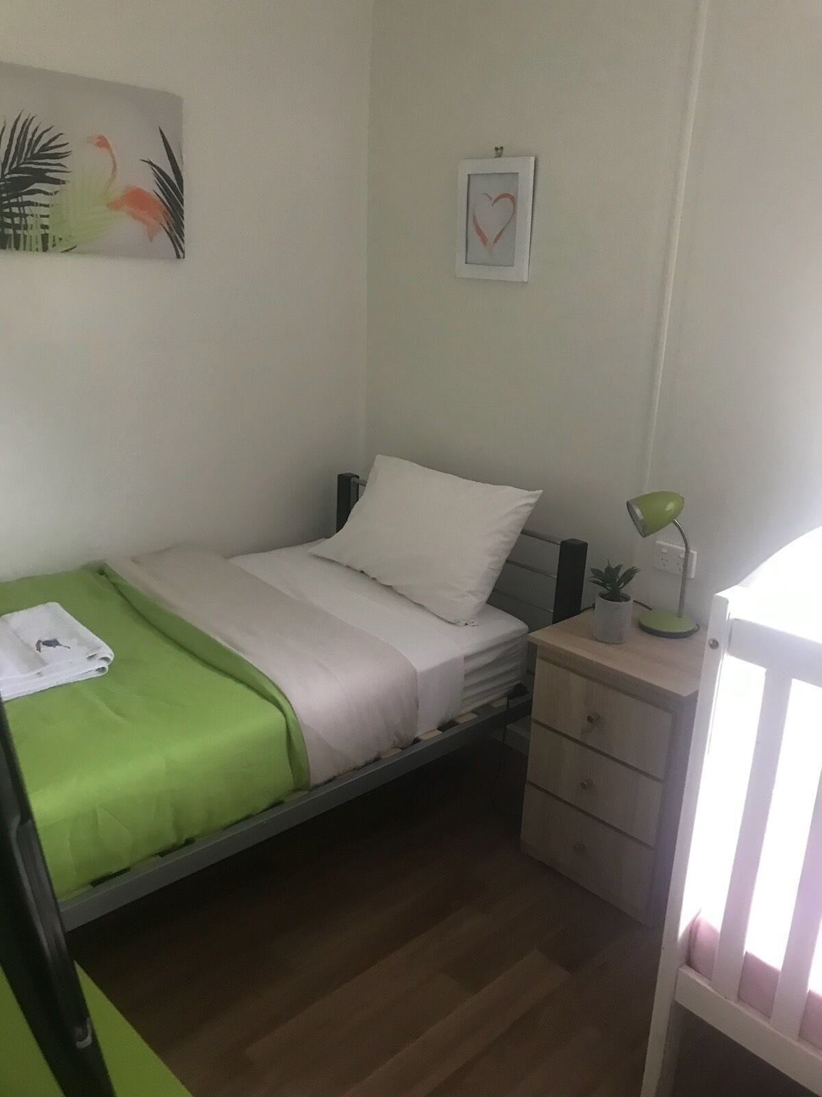 A small, neatly arranged bedroom with a single bed, a bedside table with a lamp, and a small cabinet.