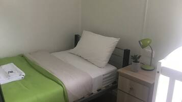 A small, neatly arranged bedroom with a single bed, a bedside table with a lamp, and a small cabinet.