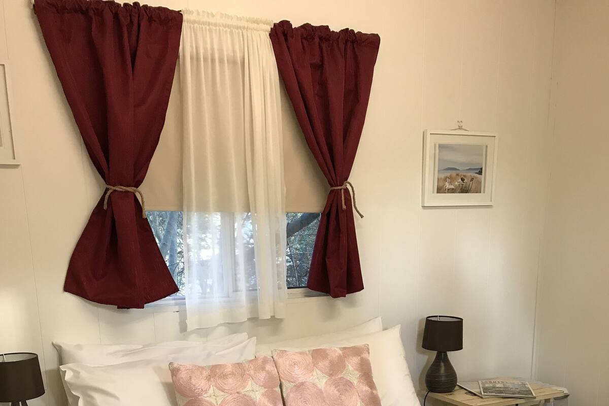 A neatly made bed with floral bedding, two bedside lamps, a small bedside table with a lamp, and a window with curtains.
