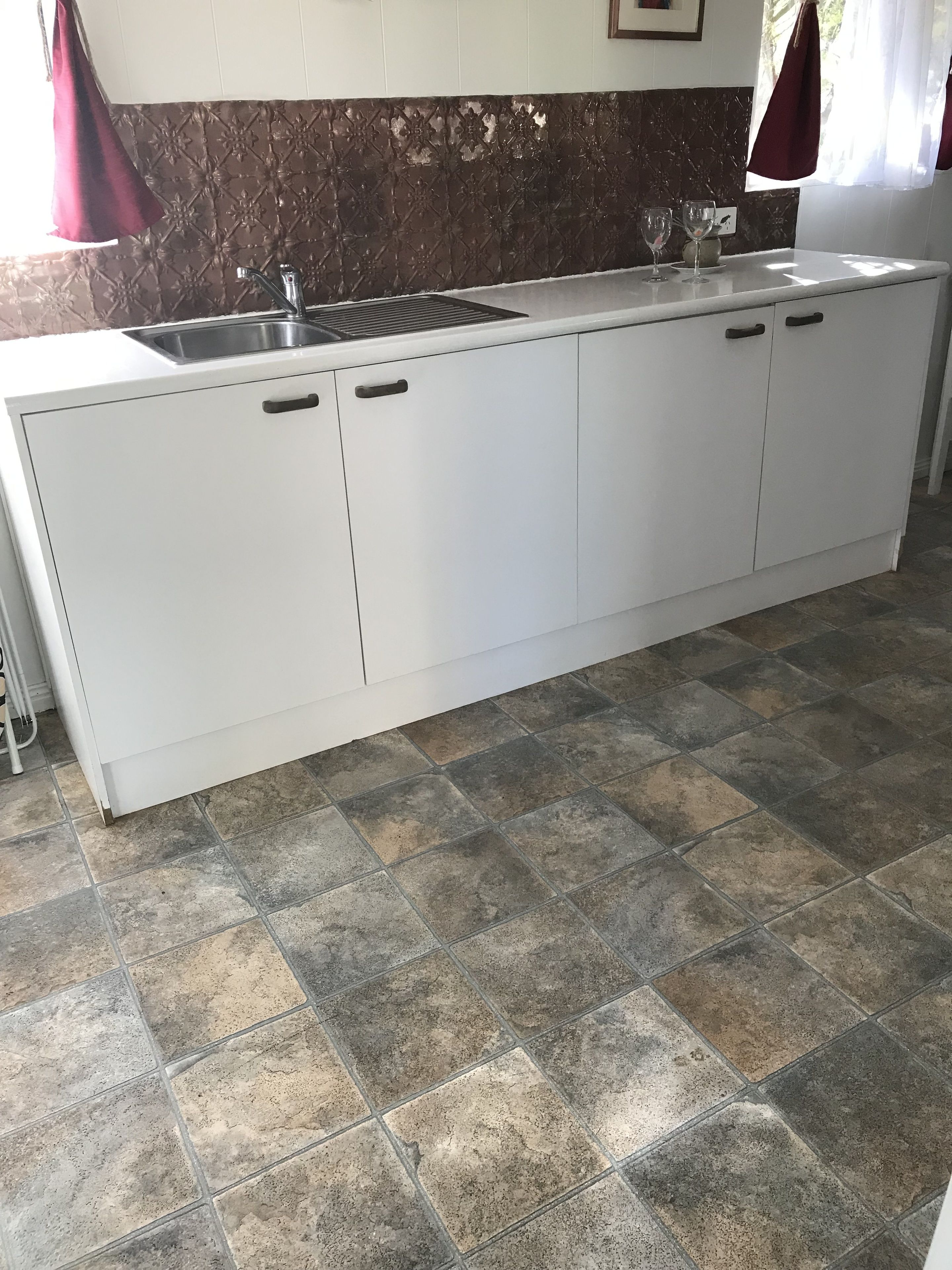 A kitchen with white cabinets, a stainless steel sink, and a tiled floor.