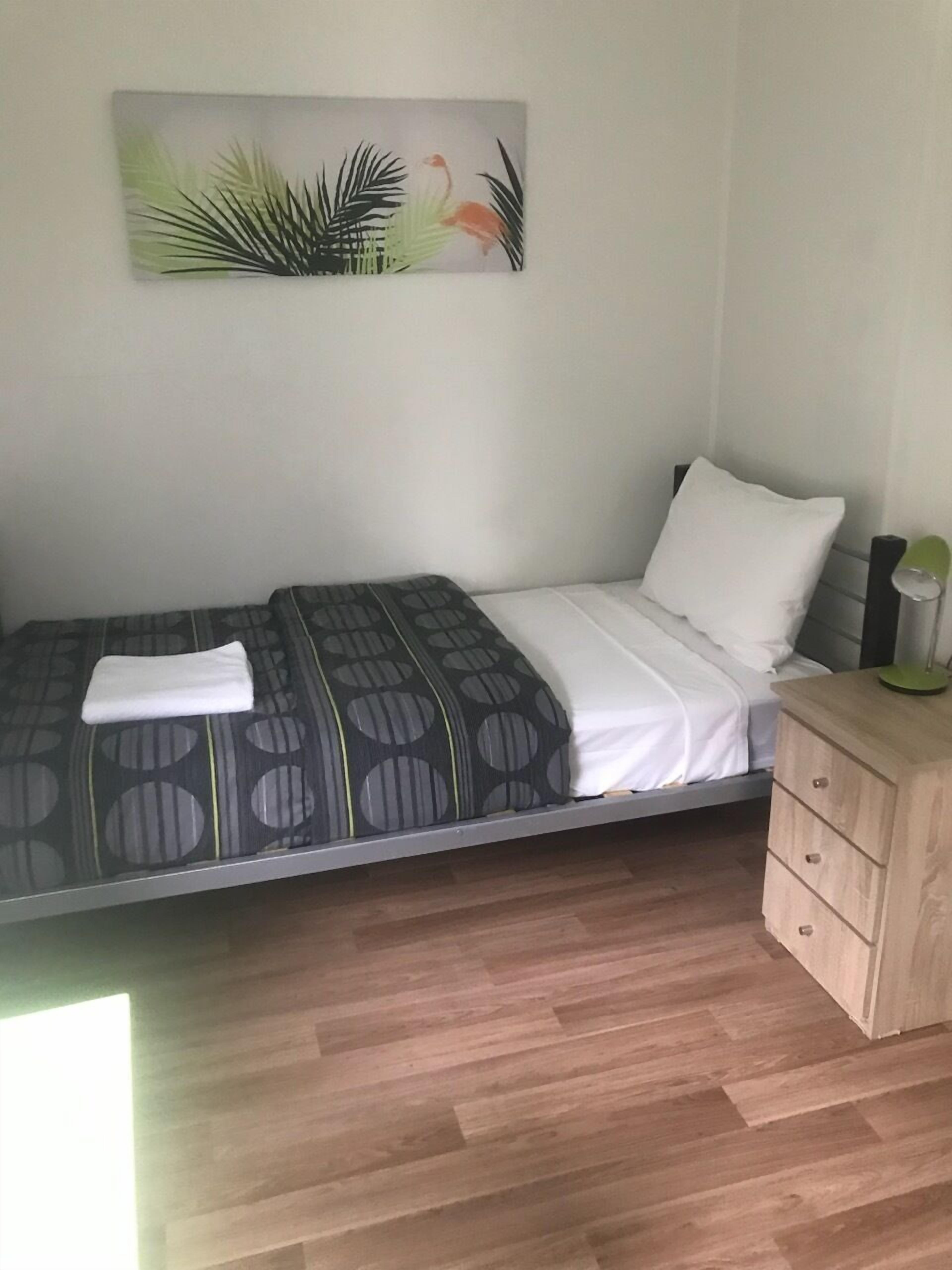 A single bed with a patterned bedspread, a white pillow, and a bedside table with drawers.