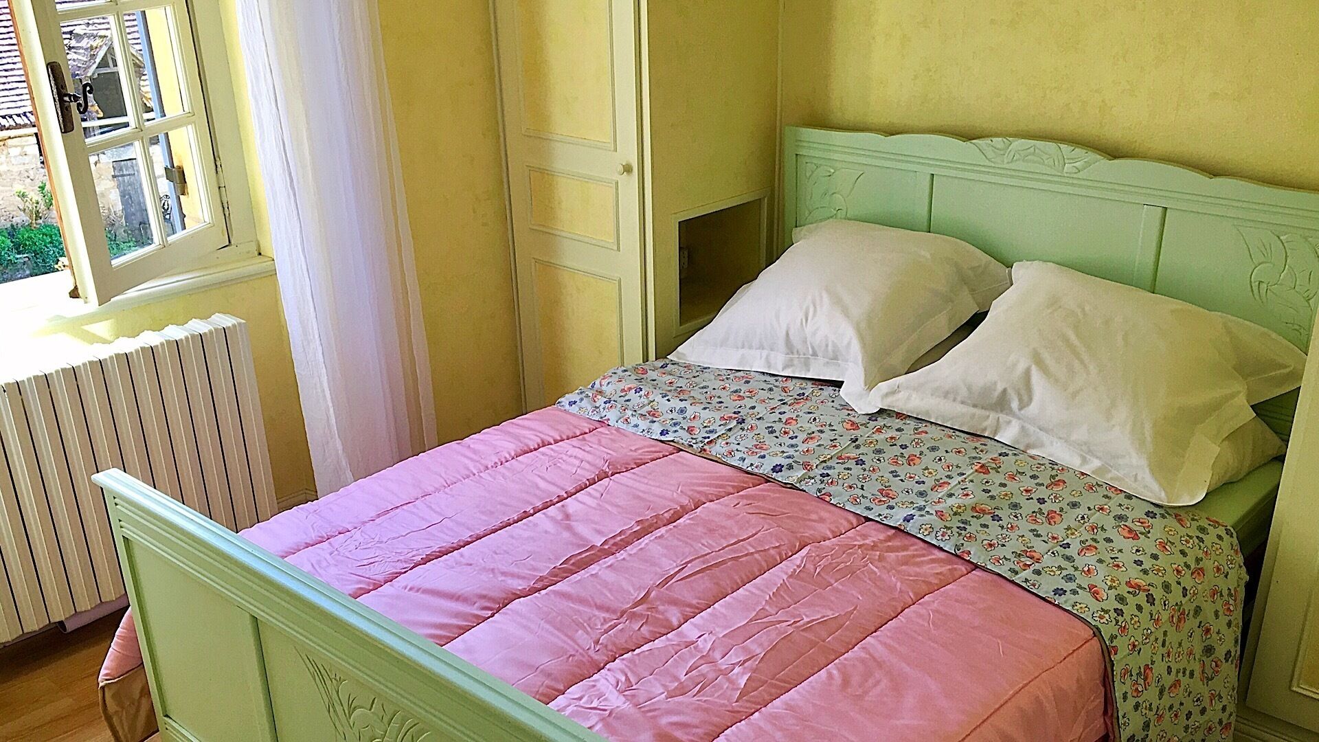 Une chambre à coucher avec un lit, un radiateur et une fenêtre avec des rideaux.