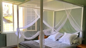 Un letto a baldacchino con tende e lenzuola bianche in una stanza con pareti verdi e una finestra.