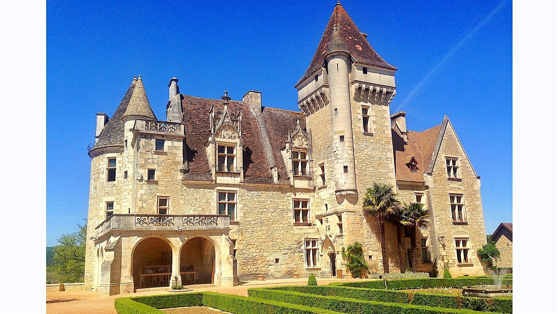Un grande edificio storico in pietra con diverse torri e finestre ad arco, immerso in giardini curati.