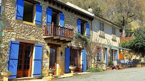 Un edificio in pietra con persiane blu, un balcone e posti a sedere all'aperto.