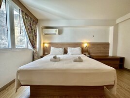 Quarto de hotel com uma cama grande, duas luminárias de cabeceira, um aparelho de ar condicionado e uma janela com cortinas.
