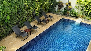 A swimming pool with tiled edges, surrounded by lush greenery and black lounge chairs. - Dinsomon (Bangkok)