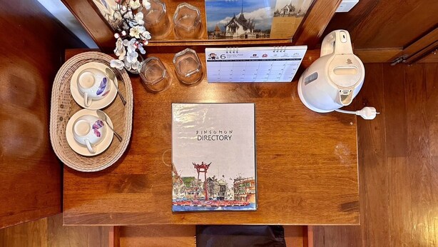 A wooden table with a book titled 'Dinsomon Directory', a calendar, a portable toilet, and a hairdryer in a drawer. - Dinsomon (Bangkok)