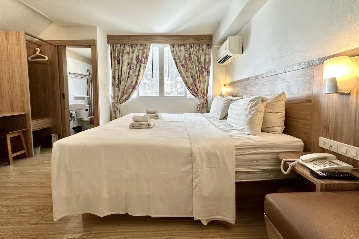 A hotel room with a bed, bedside table with a phone, and a window with curtains.