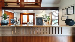 A hotel reception area with a wooden reception desk, framed certificates on the wall, and potted plants. - Dinsomon (Bangkok)