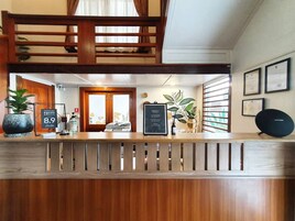 Zona de recepción de un hotel con un mostrador de madera, certificados enmarcados en la pared y plantas en macetas.