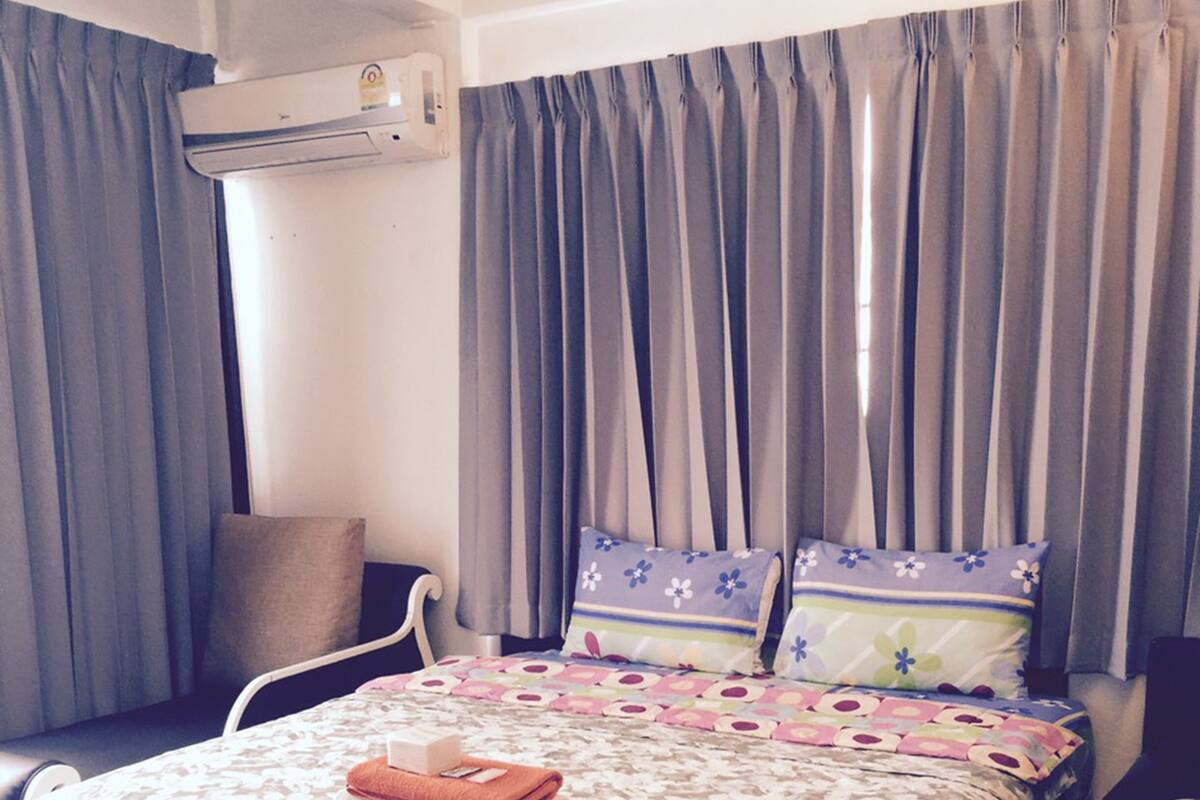 A neatly arranged hotel room with a bed, a chair, an air conditioning unit, and a window with curtains.
