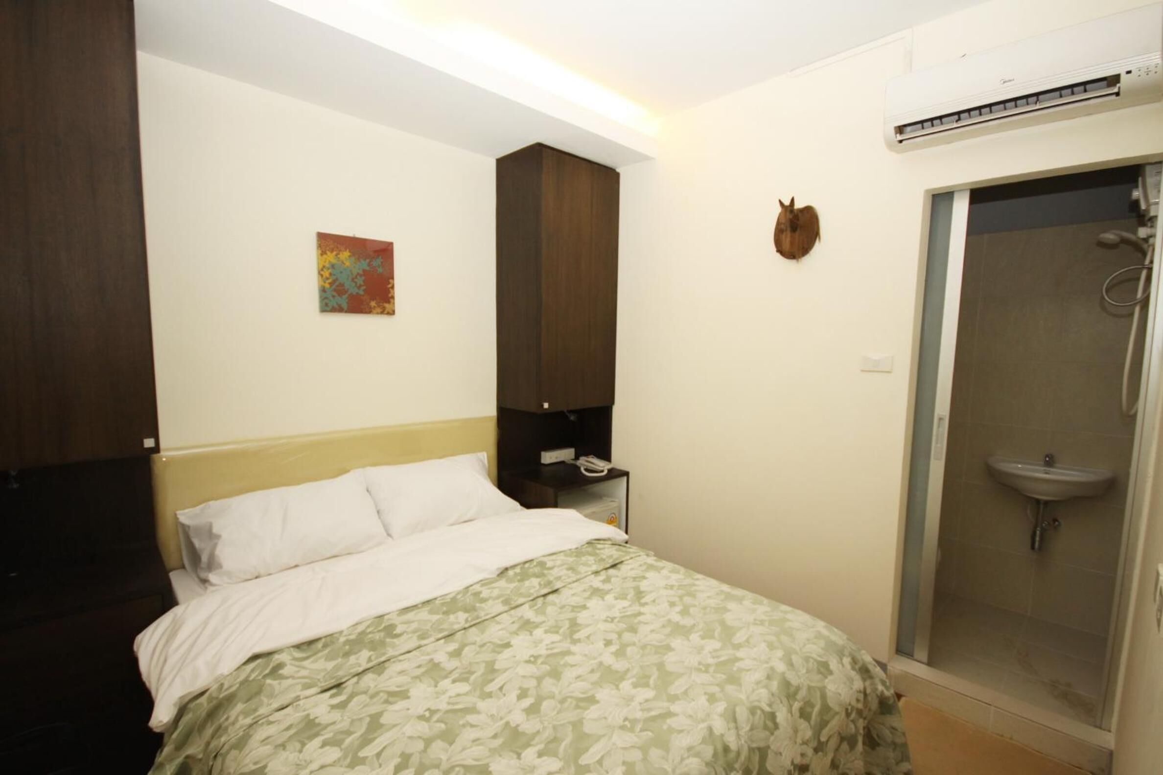 A bedroom with a bed, a nightstand, a wall-mounted air conditioner, a shower, and a small wall decoration.