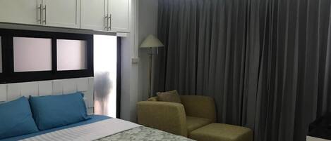 Hotellihuone, jossa on sänky, tuoli, työpöytä ja verho.