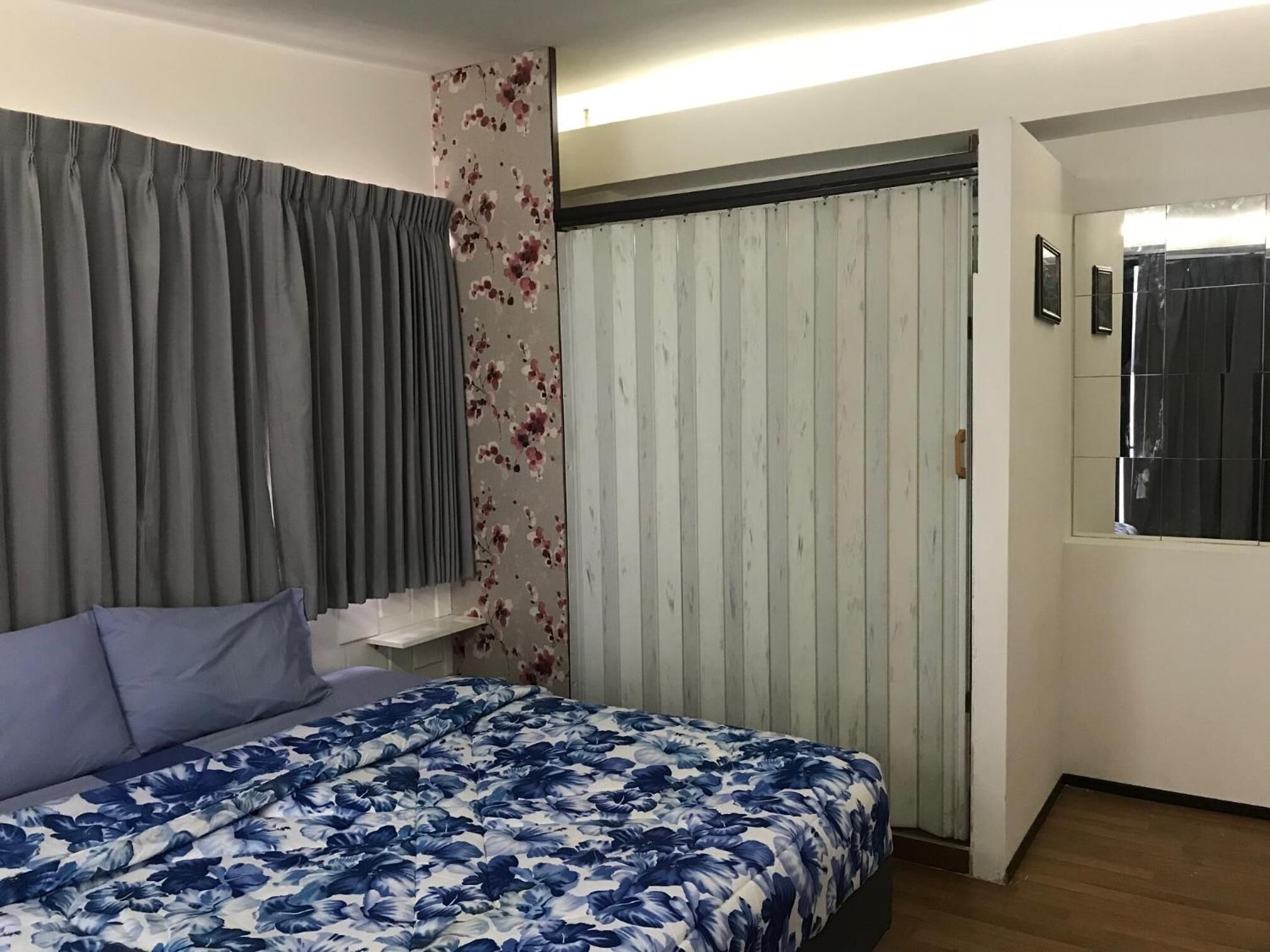 A bedroom with a bed, grey curtains, a floral-patterned wall, and a window with a black blind.
