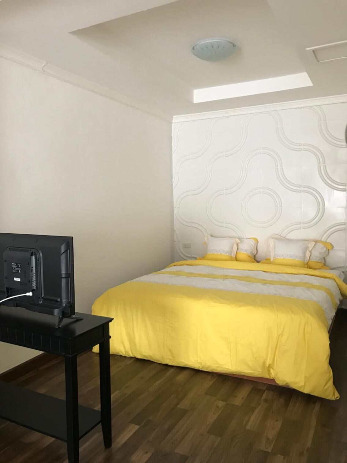 Une chambre à coucher avec un lit, un bureau avec un ordinateur et un luminaire au plafond.