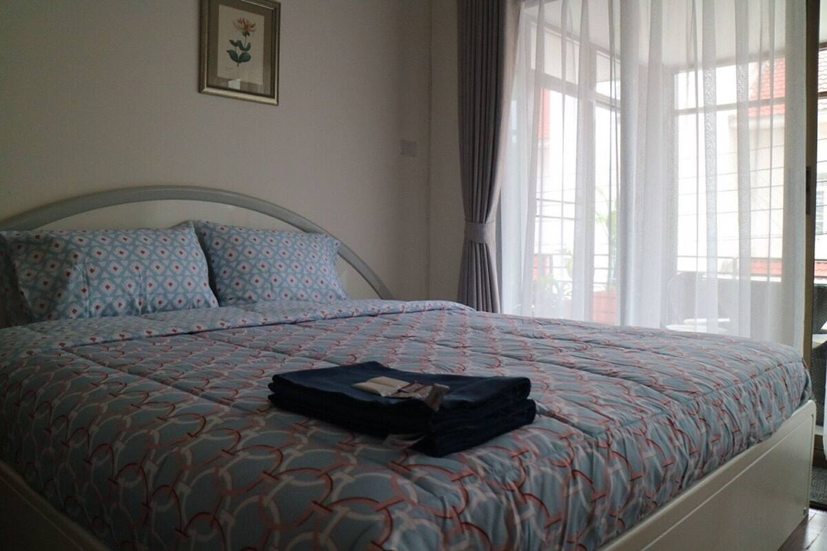 A neatly made bed with patterned bedding, a folded towel, and a framed picture on the wall.