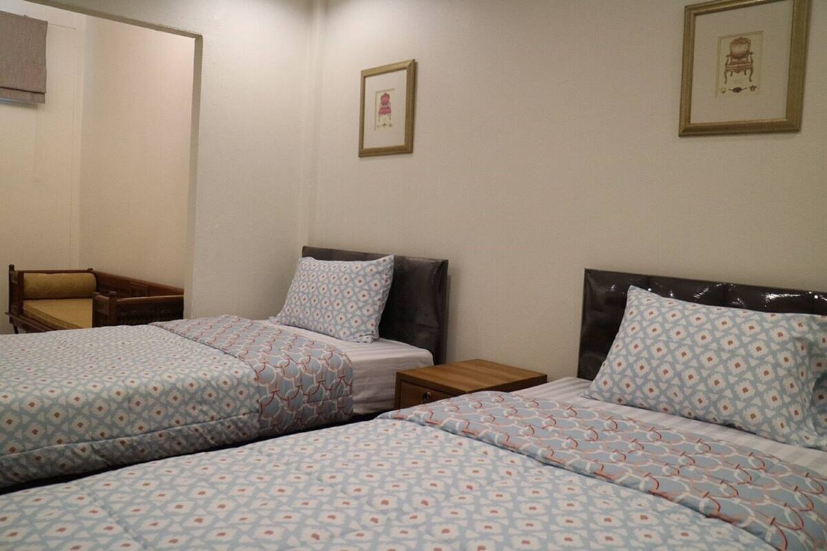 A hotel room with two beds, each with patterned bedding, a wooden nightstand, and a framed picture on the wall.