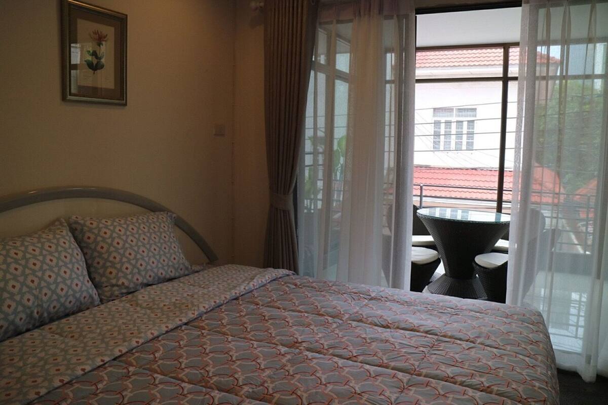 A hotel room with a bed, a framed picture on the wall, and a balcony with a table and chairs.